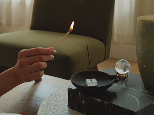 Hand lighting incense beside a crystal sphere and ritual objects