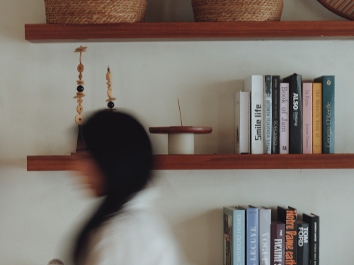 Woman walking past a shelf of books and incense