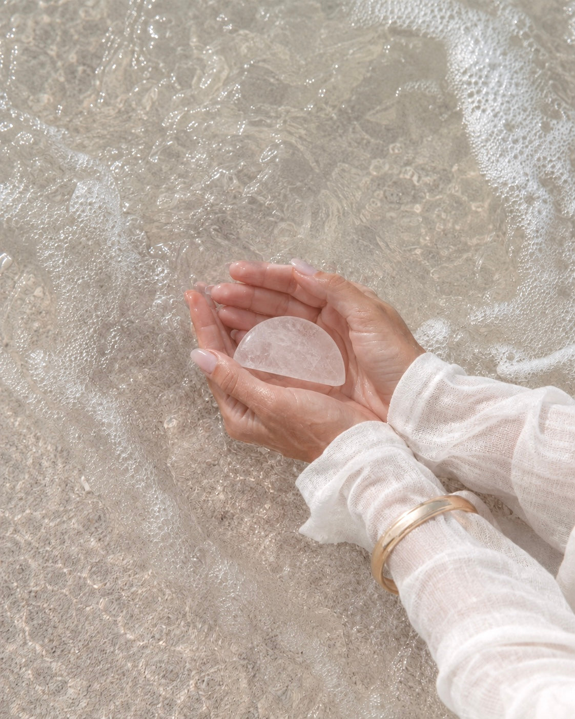 Hands holding a rose quartz stone over sand
